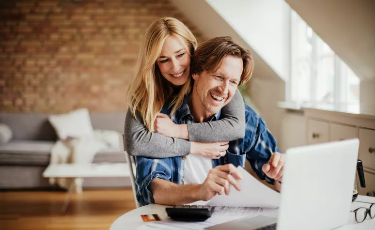 A middle-aged married couple review financial documents in front of their laptop.
